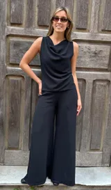 Blusa sin mangas de color negro, confeccionada en viscosa con lycra, con diseño fluido, cuello volcado y espalda descubierta con abertura vertical y lazo ajustable.