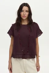Blusa de lino color beige, de manga corta con volados, cuello redondo y espalda cruzada con volados.