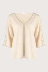 Suéter de punto color crema con cuello en V, mangas tres cuartos y detalle de costura vertical central. Presenta un diseño holgado con terminaciones acanaladas en puños y ruedo.