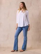 Blusa blanca de tejido labrado con cuello redondo, escote en V y aplique metálico.