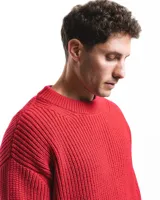 Sweater unisex de lana merino fina color rojo, con cuello redondo y corte relajado. Presenta un motivo inspirado en la técnica de zurcido visible.