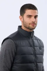 Chaleco reversible capitoneado de corte estándar, con cuello alto, cierre frontal de cremallera y botones a presión. Cuenta con bolsillos laterales y un bolsillo vertical en el pecho.