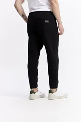 Pantalón de jogging negro de algodón y poliéster, con puños ajustados en los tobillos, cintura elástica con cordón y costuras verticales marcadas en el frente.