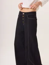 Pantalón ancho de mujer, estilo patchwork, combinando paneles de tela en tonos beige claro, beige medio y marrón. Presenta cierre frontal de botones y costuras contrastantes en rojo.