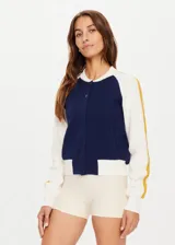 Campera bomber azul marino con mangas color crema con rayas mostaza. Tiene cuello, puños y ruedo acanalados, cierre frontal con botones a presión y corte holgado.