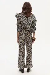 Camisa de manga larga con estampado floral, confeccionada en tejido de pana. Presenta cuello clásico, cierre frontal con botones a tono y volados decorativos que recorren el frente y la espalda en diagonal desde los hombros hasta la cintura.