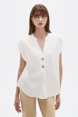 Blusa de viscosa color blanco, de corte holgado, con cuello en V y cierre frontal parcial de botones grandes con efecto carey.