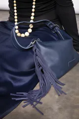 Cartera de cuero azul marino con diseño de flecos colgantes, asa corta de hombro y cierre superior con cremallera.