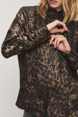 Camisa de satén con estampado animal print tipo leopardo en tonos marrones y negros. Presenta cuello alto con volados, mangas largas con puños abotonados y detalles de volados fruncidos a lo largo de la botonadura frontal.