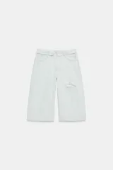 Bermuda tipo jorts de denim en color celeste claro, con tiro medio, diseño de cinco bolsillos y cinturilla doblada. Presenta roturas decorativas en la parte delantera y cierre frontal con cremallera y botón metálico.