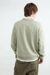Buzo de cuello redondo color verde militar, de corte holgado, mangas largas y diseño liso.