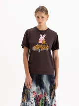 Remera de algodón pima color marrón, con estampa frontal de un conejo rosa sobre un auto con diseño de leopardo. Presenta cuello redondo y mangas cortas.