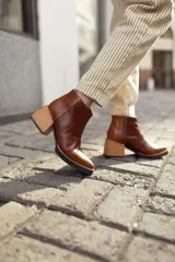 Botineta de cuero color suela, con diseño de punta fina y puntera texturizada con efecto reptil. Presenta una suela de madera clara con borde negro y cierre lateral interno.