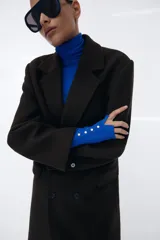 Jersey de punto liso en color beige, con cuello alto y manga larga con detalle de botones metálicos en los puños.