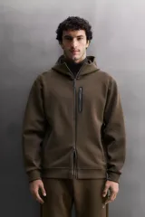 Sudadera con capucha de entrenamiento, confeccionada en tejido técnico de algodón con efecto neopreno. Presenta cierre frontal de cremallera, cuello subido, bolsillos laterales y un bolsillo en el pecho, todos con cierre de cremallera y acabado termofijado.