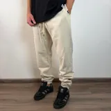 Pantalón tipo jogger de friza de algodón en color beige, con cintura elástica ajustable mediante cordón y puños elásticos en los tobillos. Presenta un calce holgado y cómodo.