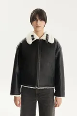 Campera corta estilo aviador de cuero sintético negro con cuello de piel sintética blanca, cierre frontal con cremallera, bolsillos laterales y puños y bajo acanalados.