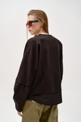 Camiseta oversize de cuello redondo y manga larga con puños abotonados. Confeccionada en algodón, presenta un diseño con combinación de tejidos a tono y bajo asimétrico.