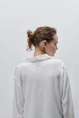 Camisa de viscosa color celeste, de calce amplio y caída fluida, con cuello clásico, cierre frontal de botones y detalles calados en mangas y delantero.