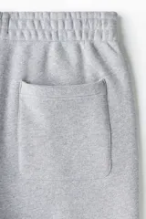 Pantalón deportivo de felpa de mezcla de algodón en color gris melange, con corte relajado, cintura elástica y puños ajustados en los tobillos. Cuenta con bolsillos laterales y cierre decorativo.