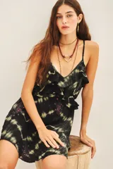 Vestido corto negro con estampado tie-dye en tonos beige/amarillento. Presenta escote en V con volados en el frente y tirantes finos ajustables. Tiene bordados con cuentas en tonos rosados/rojizos en la parte inferior.