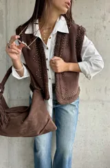 Chaleco de gamuza color chocolate con interior y bordes de corderito sintético. Presenta diseño con tachas metálicas decorativas en el frente y los hombros.