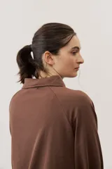 Buzo celeste de manga larga con cuello polo y cierre frontal de botones. Presenta un parche marrón bordado en el pecho.