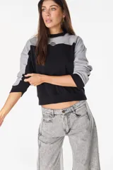 Buzo de cuello redondo con diseño de bloques de color en gris y negro, mangas largas y detalle bordado en el pecho.