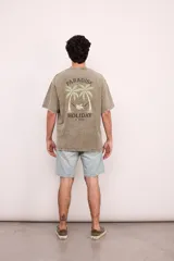 Remera negra con efecto gastado, corte oversize, mangas cortas y estampa en la espalda con palmeras, ángel en una hamaca y texto "Paradise Holiday Brixton".