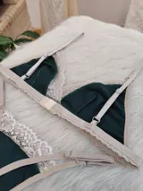 Conjunto de lencería compuesto por bralette triangular y tanga, confeccionado en algodón color verde inglés con detalles de encaje en tono nude. El bralette cuenta con breteles ajustables y broche regulable, mientras que la tanga presenta laterales ajustables.