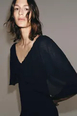 Vestido largo de punto color negro, con escote en V pronunciado tanto en el delantero como en la espalda, y mangas cortas anchas con vuelo.
