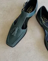 Mocasín negro de cuero vacuno, con punta cuadrada y detalle de borlas en el empeine.