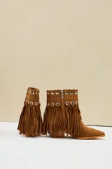 Bota texana de gamuza color camel, con taco cuadrado y punta fina. Cuenta con flecos largos colgantes y detalles de ojalillos metálicos plateados en la parte superior.