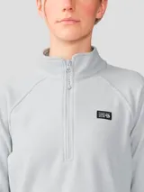 Buzo polar de mujer con cierre frontal de un cuarto, cuello alto y mangas raglán. Presenta un diseño minimalista en color gris claro con el logo de la marca bordado en el pecho.