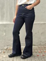 Jean de tiro alto en denim azul oscuro, con corte ajustado en la parte superior y levemente oxford en la botamanga. Presenta costuras verticales visibles a lo largo de la pierna que estilizan la silueta.