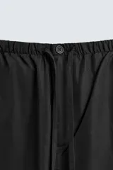 Pantalón de corte relajado confeccionado en tejido fluido con mezcla de lyocell. Presenta cintura elástica ajustable con cordón, bolsillos laterales y un bolsillo trasero de vivo con botón.