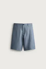Bermuda relaxed fit confeccionada en lino color celeste, con bolsillos laterales, bolsillos traseros de vivo y cierre frontal con cremallera y botón.