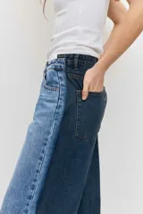 Jean wide leg de tiro medio, confeccionado en denim azul con detalles de paneles laterales en un tono más oscuro, tiro medio, cierre frontal con botón y cremallera, y diseño de perneras amplias.