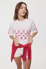 Remera blanca de manga corta, con cuello redondo, calce relajado y estampado frontal con motivos gráficos de soles y símbolos marinos en tonos rosados y bordo, además de líneas horizontales.