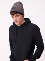 Gorro tipo beanie de punto color negro con diseño gráfico circular en gris en la parte frontal.