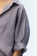 Camisa oversize blanca de lino, con corte cuadrado, mangas raglán cortas con puños anchos, aberturas laterales y cierre frontal de botones.