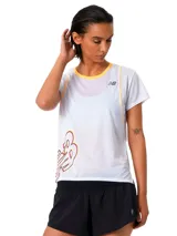 Remera deportiva blanca para mujer, de manga corta, con cuello redondo en tono amarillo y un gran estampado del logo de New Balance en el lateral inferior.
