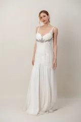 Vestido largo de gasa color marfil, con escote en V, drapeado en el torso y detalle de bordado en pedrería bajo el busto, falda amplia tipo godet y tiritas anchas.