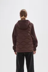 Campera con capucha de diseño híbrido, combinando un panel frontal acolchado con diseño ondulado y mangas de tejido liso. Cuenta con cierre frontal completo, puños elásticos y bolsillos laterales.