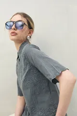 Camisa blanca de manga corta confeccionada en algodón, con bordados a tono y terminaciones festoneadas. Presenta cuello clásico y silueta recta.