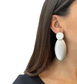 Aros colgantes con forma geométrica, con un círculo pequeño color crema en la parte superior y una forma ovalada grande color dorado en la parte inferior.