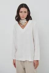 Blusa de manga larga con escote en V, confeccionada en tejido liviano de color crudo con textura sutil.
