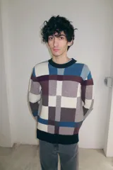Sweater de cuello redondo con diseño jacquard a cuadros en tonos azul, marrón, blanco y negro. Presenta un ajuste holgado y puños, cuello y ruedo acanalados.