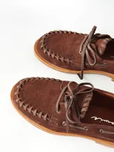 Sandalias de cuero gamuzado color marrón chocolate, diseño tipo huarache con tiras entrelazadas, tira en el empeine, talón cerrado y hebilla metálica de ajuste lateral.