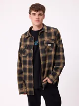 Camisa de manga larga confeccionada en franela de algodón, con diseño de cuadros en tonos verde y marrón. Presenta cuello clásico, cierre frontal con botones y dos bolsillos en el pecho con solapa.